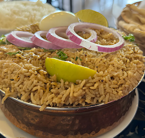 Biryani rice in a copper pot topped with onion rings, lime wedges, and a boiled egg