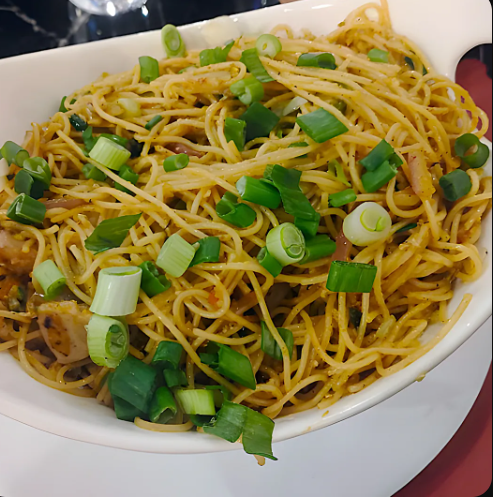 Stir-fried noodles topped with chopped scallions in a white bowl
