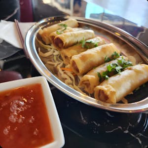 Fried spring rolls on a stainless steel platter with dipping sauce