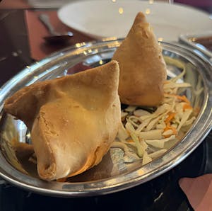 Two samosas on a stainless steel plate with shredded cabbage