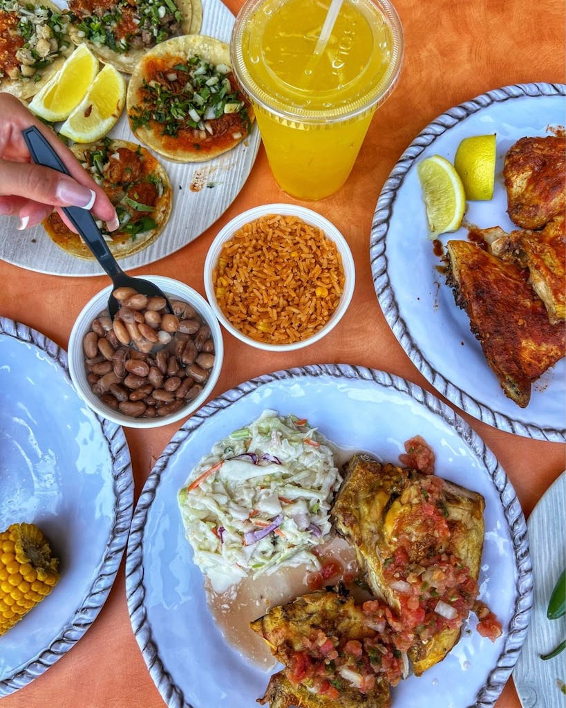 Tacos, grilled chicken with lemon, rice, pinto beans (hand spooning), coleslaw, corn, and a yellow drink.