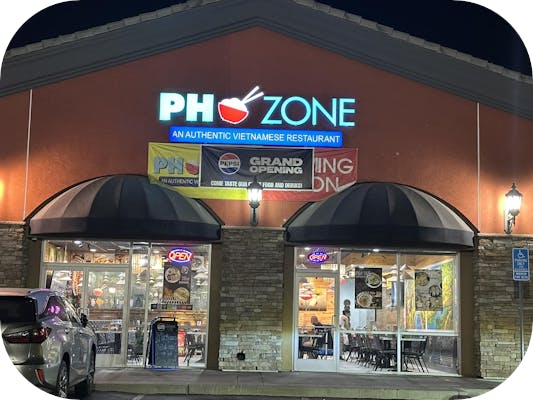Pho Zone storefront in Highland, CA at night with neon sign and grand opening banner.