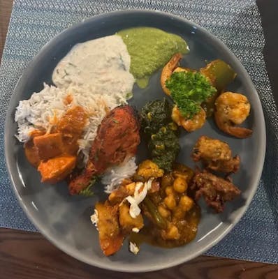 Basmati rice plate with raita and mint chutney, tandoori chicken, tikka masala, saag, shrimp, chana masala, and vegetable pakoras.