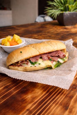 roast beef sandwich, specifically a hot melt or French dip style, served on a toasted long roll with a side of fruit. 