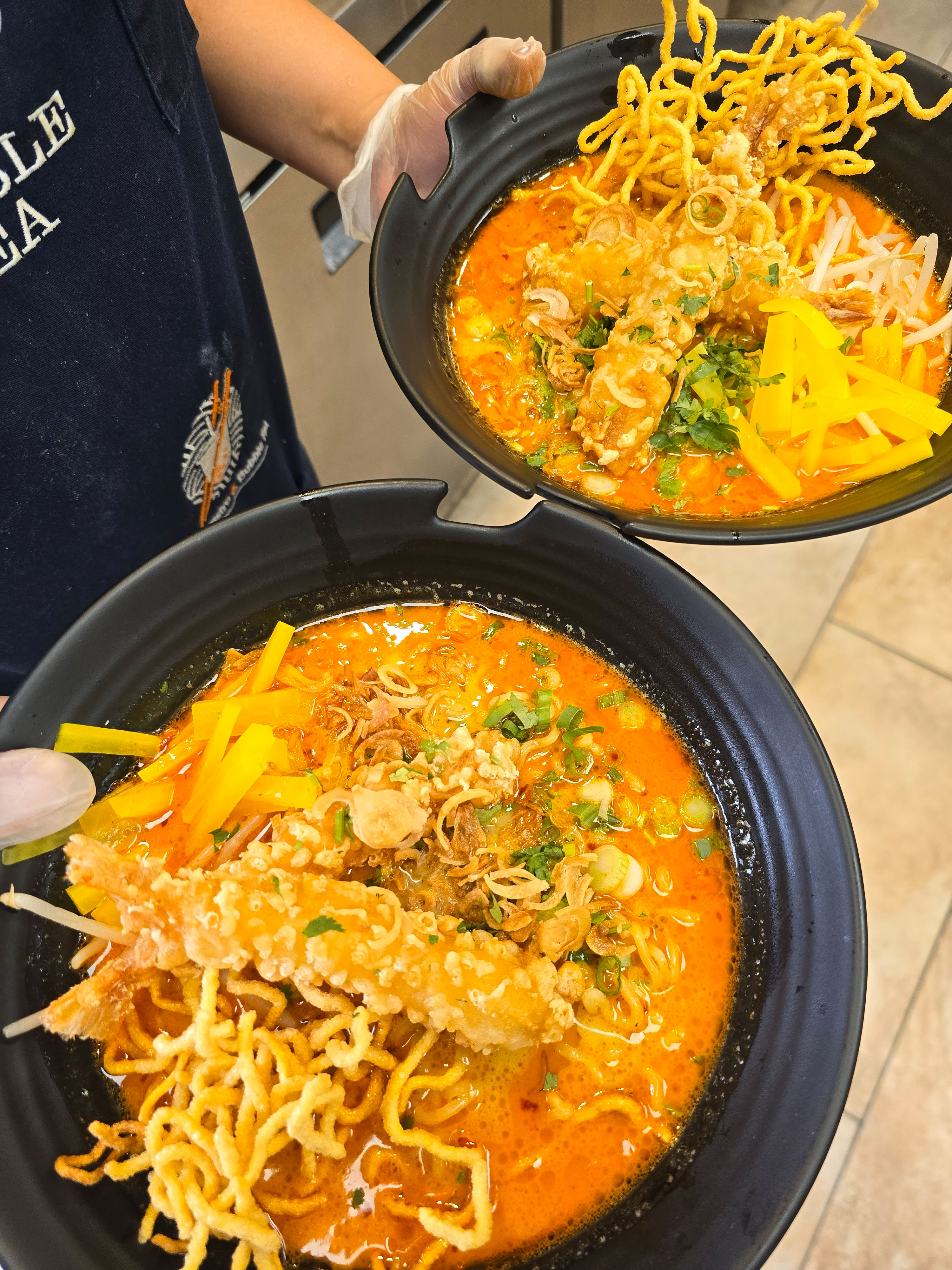 Spicy-curry-noodle-soup-topped-with-crispy-fried-noodles,-tempura-style-shrimp,-scallions,-fried-shallots,-and-pickled-veggies-bean-sprouts
