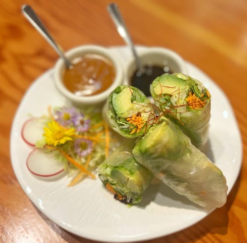Fresh vegetable spring rolls with avocado, lettuce and carrots, served with peanut and hoisin sauces, radish slices and edible flowers