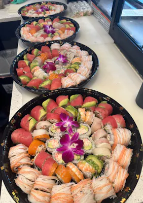 Row of round sushi platters with assorted rolls, crab salad, and purple orchids