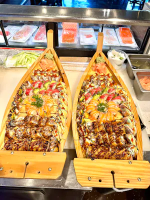 Two wooden sushi boats loaded with assorted rolls and sashimi