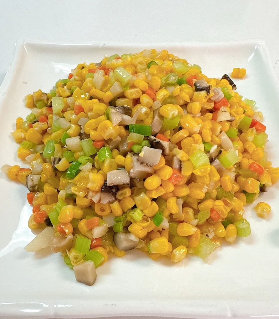 Stir-fried sweet corn with diced celery, carrots, scallions, and mushrooms on a white plate